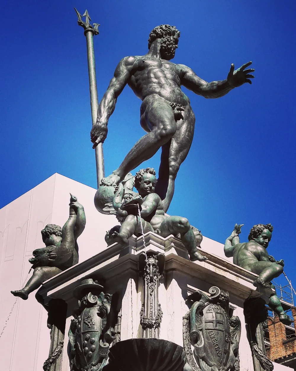 Fotografia a colori della statua del Nettuno a Bologna: il tridente, la mano aperta e le figure della fontana contro il cielo blu.